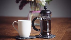 Close-Up Of Coffee Cup And French Press On Table