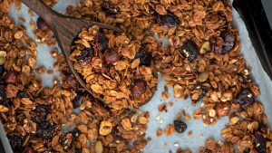 Müsli: Granola auf einem mit Backpapier ausgelegtem Backblech zusammen mit Rosinen und Nüssen