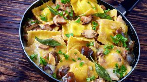 delicious ravioli stuffed with ricotta cheese cooked in creamy garlic mushrooms sauce in a skillet on an old wooden table, view from above, close-up