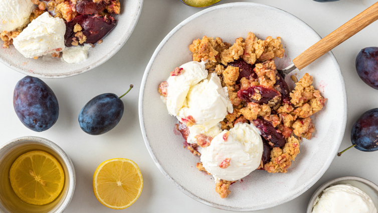 Zwetschgen-Crumble auf einem Teller mit einer Kugel Vanilleeis.