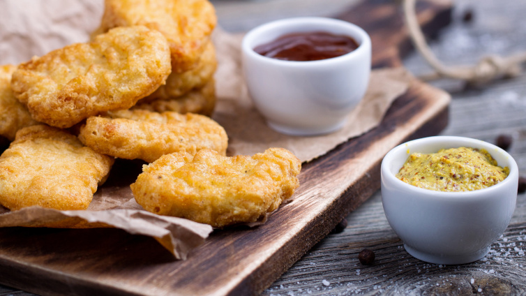 Chicken Nuggets liegen auf einem Brett neben zwei Schälchen mit Ketchup und Senf.