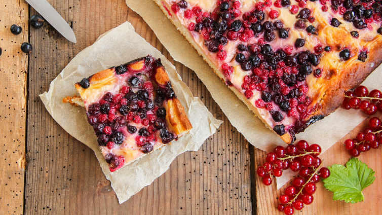 Ein Blechkuchen mit Johannisbeeren neben frischen Johannisbeeren.