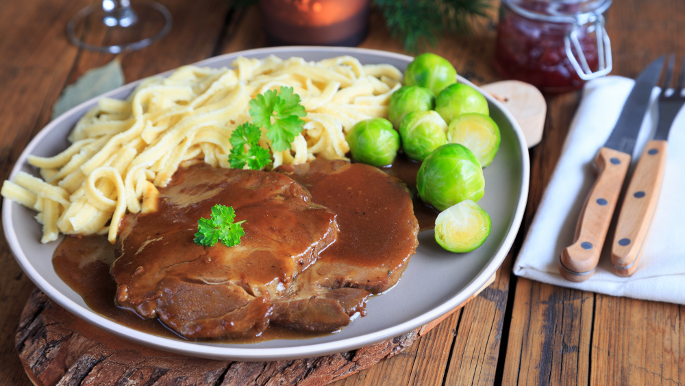 Wildschweinbraten mit Spätzle, Rosenkohl und Bratensauce auf einem Teller.