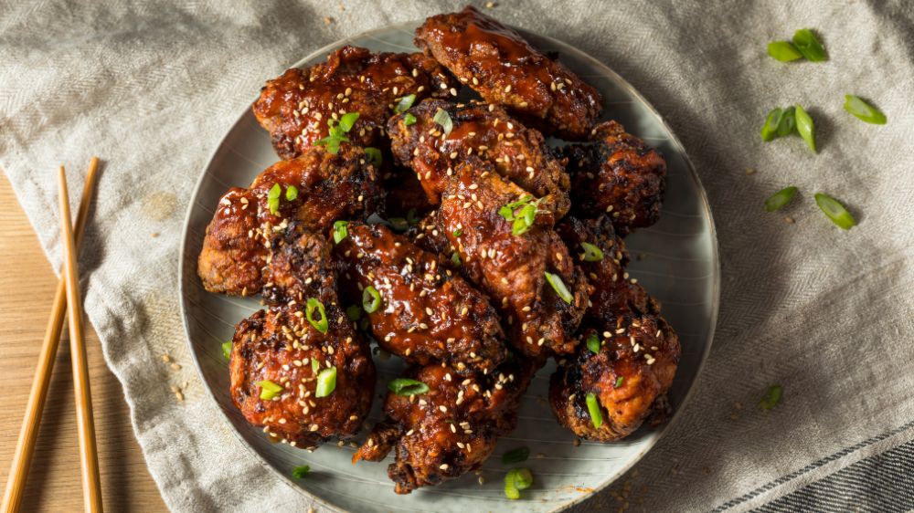 Korean Fried Chicken mit Sesam und Frühlingszwiebeln auf einem grauen Teller.