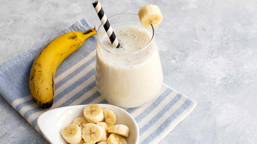 Bananen-Milchshake mit frischen Bananen und Strohhalm angerichtet.